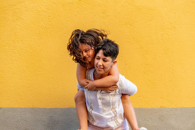 Happy woman standing against yellow wall