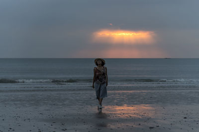 Woman standing on beach against sky during sunset