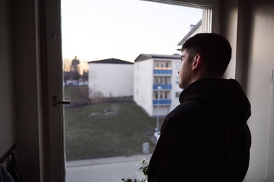 Thoughtful young man looking through window