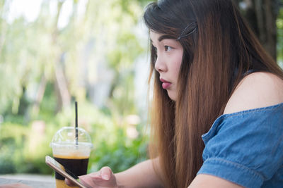 Young woman holding mobile phone by drink at table