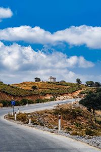 Road by buildings against sky