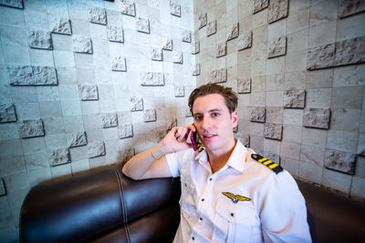 Portrait of young man using mobile phone against wall