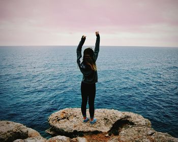 Rear view of woman standing on rock by sea against sky