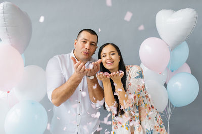 Happy couple in love blowing on confetti in honor of their love on the background of balloons