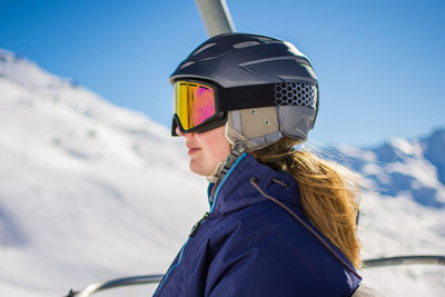 Woman wearing ski goggles and helmet while sitting in ski lift against sky