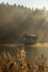 House by lake and trees against sky