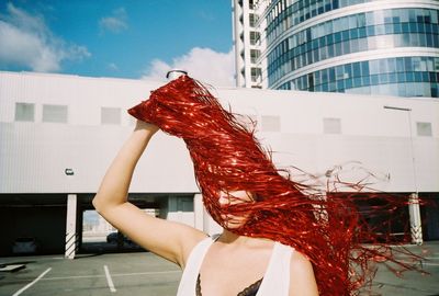 Woman covering face with pom-pom while standing against buildings