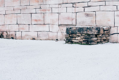 A stoned bench front a wall and a snowy ground