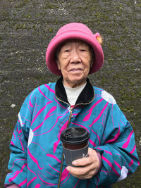 Portrait of senior woman holding coffee cup against wall