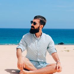 Young man sitting at beach during sunny day