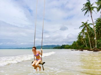 Beautiful woman wearing bikini while sitting on swing at beach