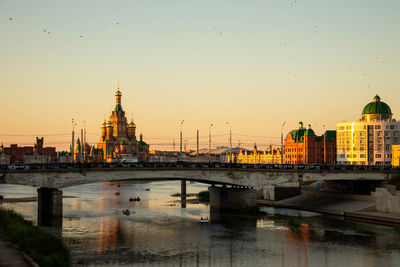 Bridge over river in city against sky during sunset