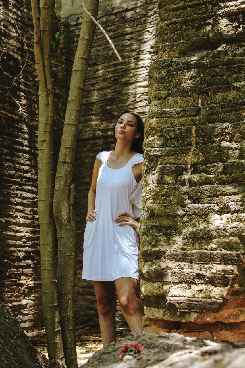 FULL LENGTH OF WOMAN STANDING AGAINST TREE TRUNK IN FOREST