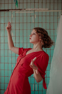 Young woman in red dress gesturing while standing at home