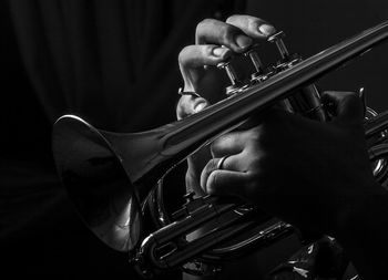 Cropped hand playing trumpet against black background