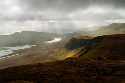 Light beams shining on vast golden valley and river with dramatic sky on isle of skye scotland.