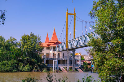 Bridge over river by building against clear blue sky