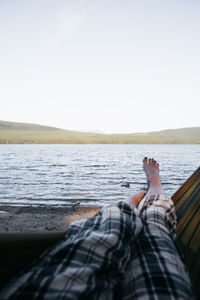 Low section of man sitting on beach against clear sky