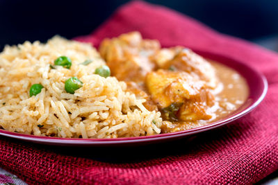 Close-up of rice with curry in plate on maroon fabric