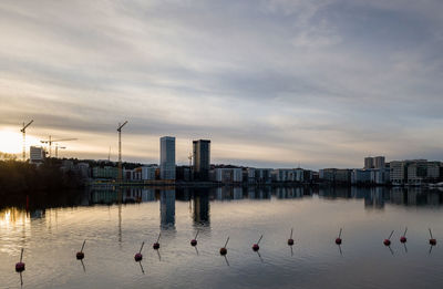 Cityscape with reflection in lake against sky during sunset