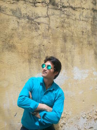 Young man with arms crossed standing against wall