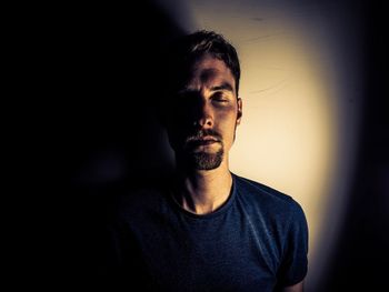 Man standing with eyes closed against wall in room