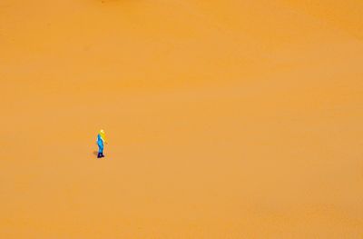 Man with umbrella on beach against orange sky