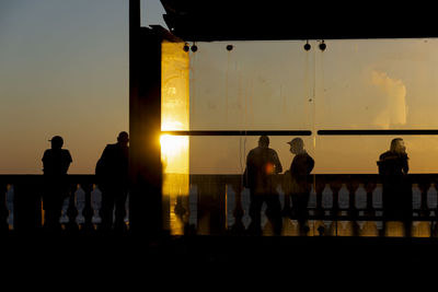 Silhouette people standing by railing against sea during sunset