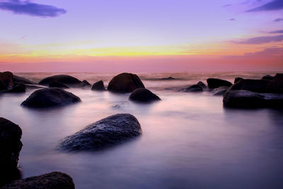 Rocks in sea against sky during sunset