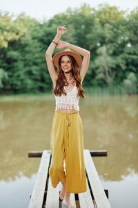 Side view of woman with arms raised standing against trees