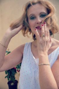 Portrait of happy mature woman with hands in hair against wall