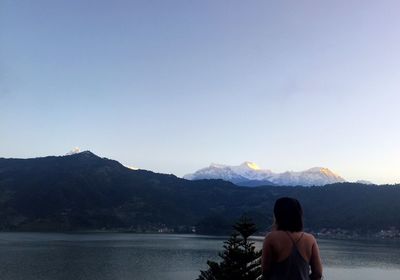 Rear view of woman by lake against clear sky