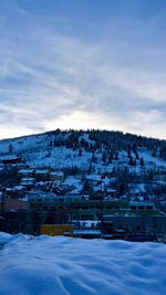 Houses on snow covered field by buildings against sky