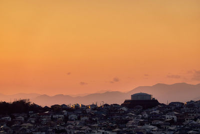 Silhouette buildings in town against orange sky