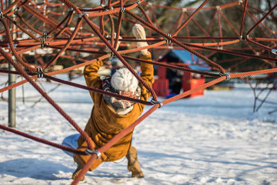 Full length rear view of woman climbing on ropes at snow covered park