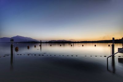 Wooden posts in lake against sky at sunset