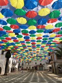 Low angle view of multi colored umbrellas hanging on street amidst buildings in city