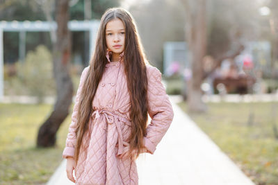 Stylish kid girl 10-12 year old wear jacket with long blonde hair standing in park. autumn season