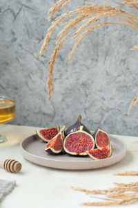 Fresh ripe slices of figs on stylish beige ceramic plate, bowl with honey and honey stick