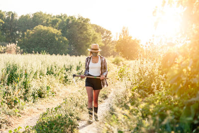 Farmer with axe wearing mask while walking by plants against clear sky