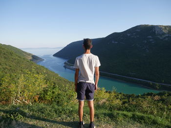 Rear view of man standing on mountain against sky