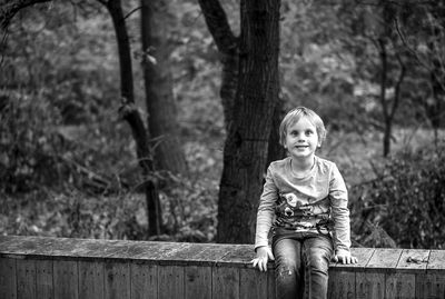 Portrait of cute boy sitting on railing against trees