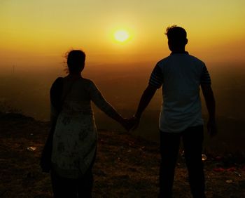 Rear view of friends standing on land during sunset