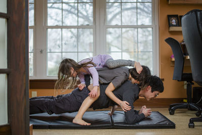 A father holds a plank position with two children piled on his back
