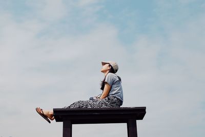 Low angle view of woman sitting on seat against sky