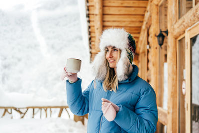 Gorgeous young woman enjoying a frosty winter day with a drink outside in the mountains.
