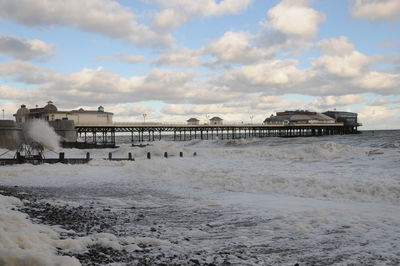 View of pier on beach against cloudy sky