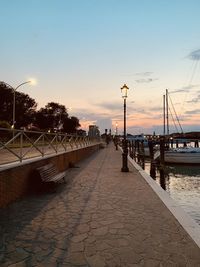 Footpath by street against sky during sunset