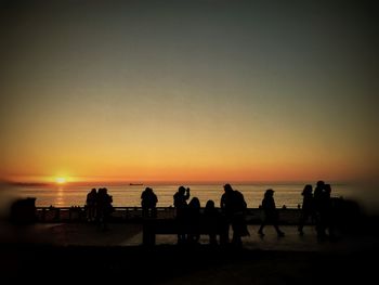 Silhouette people on beach against orange sky