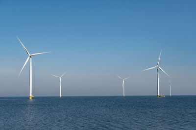 Wind turbines in sea against clear blue sky